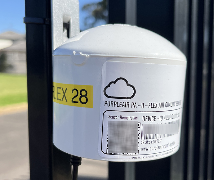 A small white box with a sticker that says 'purple air', attached to a fence