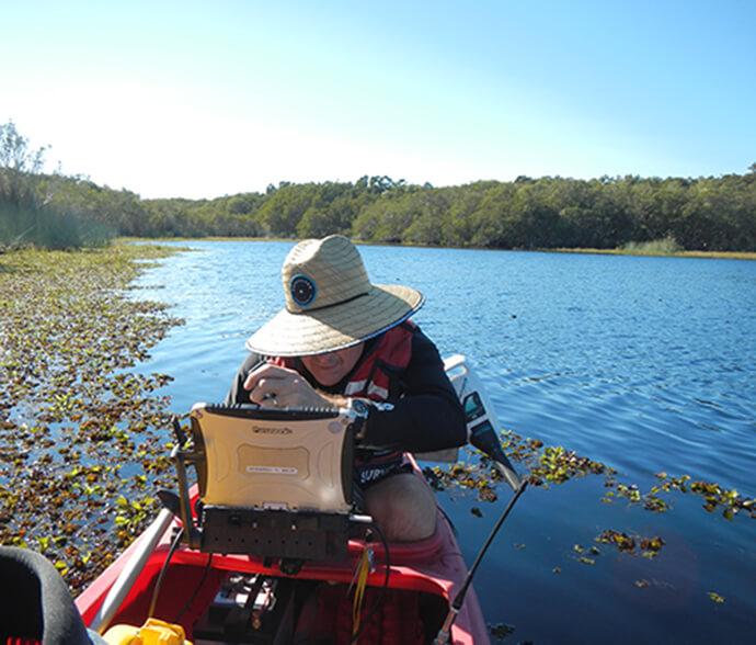 Hydrographic surveyor surveying Goolawah Lagoon at Crescent Head using an echosounder mounted on a canoe.