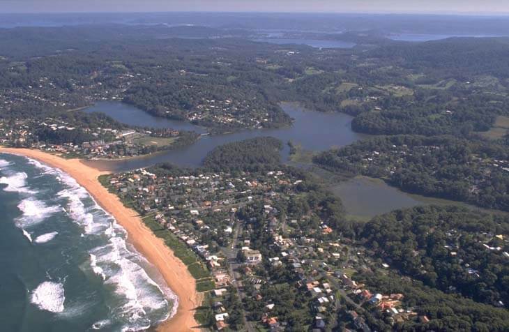 A view of Avoca Lake surrounded by coastal suburbs, wooded hills and white-sandy beaches