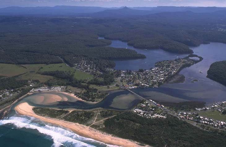 A view of Burrill Lake meeting the sea surrounded by the coastal suburbs and Burill Beach in the foreground 