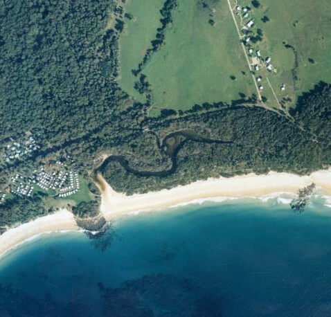 A view of Butlers Creek meeting the sea surrounded by tree-lined landscape and Shelly Beach in the foreground