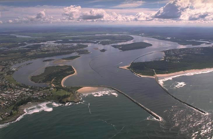 A view of Clarence River flowing through a breakwater into Shoal Bay flanked by the town of Yamba and the village of Iluka