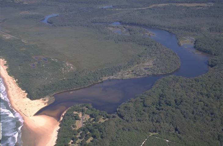 Aerial view of Khappinghat Creek winding through a forested area and flowing into the ocean, with a sandy beach on one side.