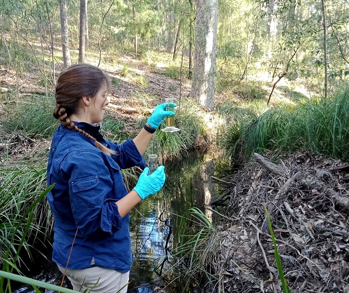 Person standing in creek taking a water sample