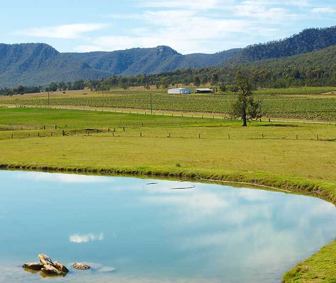 Acres of green grass beside a large dam, there are mountain ranges in the background.