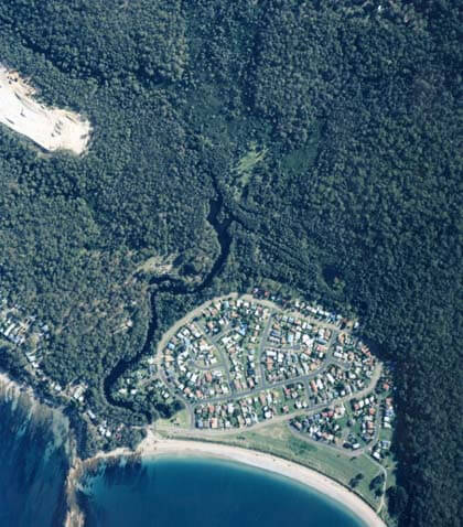 Aerial view of Maloneys Creek estuaries, with dense greenery, showing a curved shoreline on the bottom edge and a river winding through the forest from the top center.