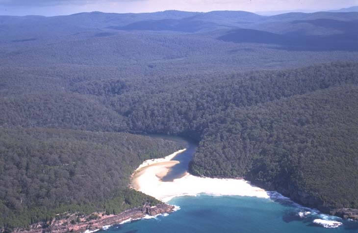 Aerial view of Merrica River flowing through dense forests into a turquoise sea with visible sandbanks at its mouth.