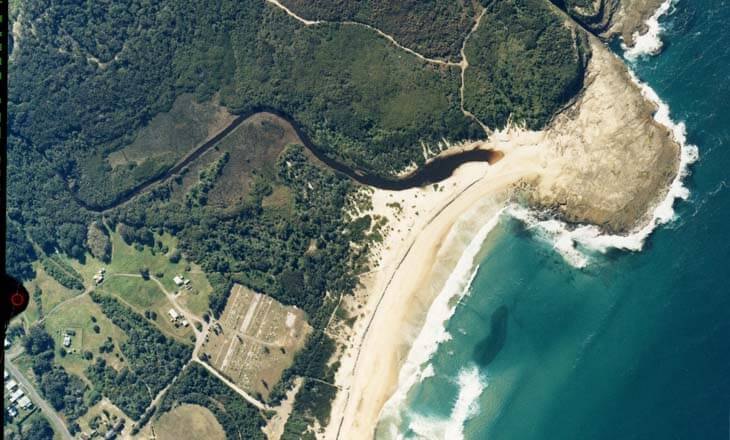 Aerial view of Middle Camp Creek flowing through dense forests into a turquoise sea with visible sandbanks at its mouth.