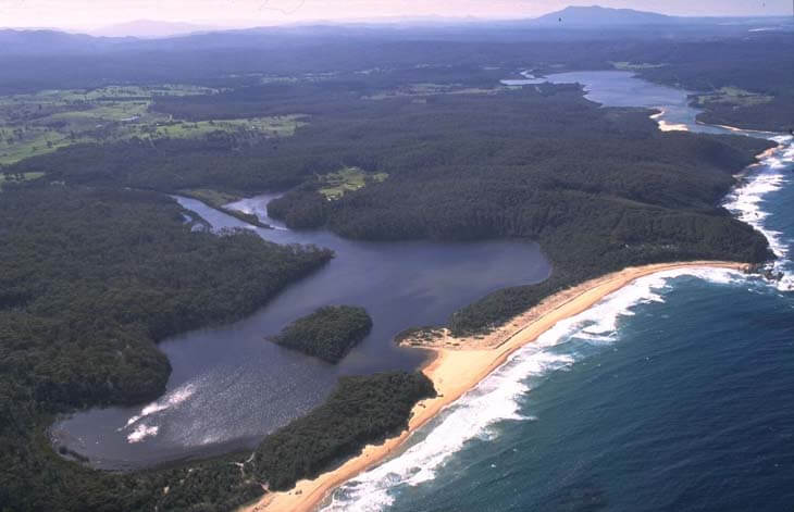 Aerial view of Middle Lagoon flowing through dense forests into a turquoise sea with visible sandbanks at its mouth.