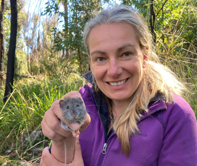 Anna is out in the field holding up a native mouse and looking at the camera