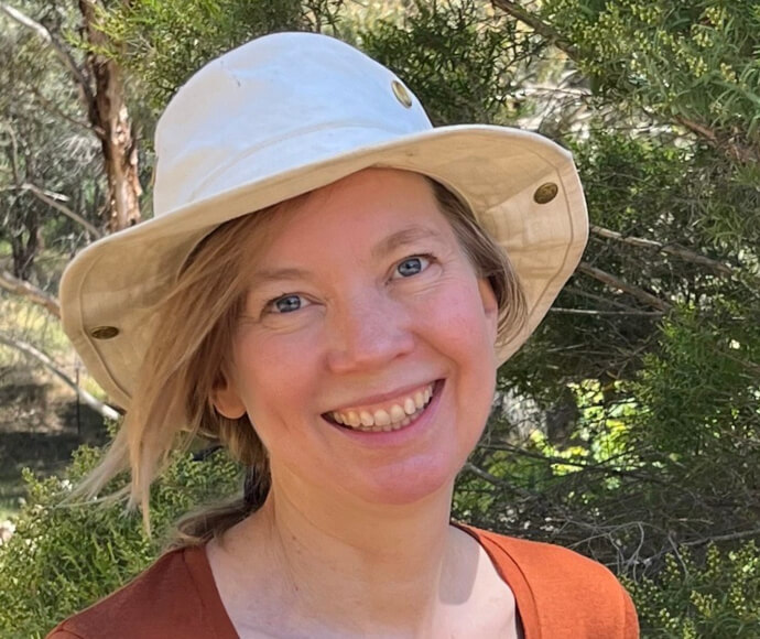 Anna stands in front of native trees, smiling