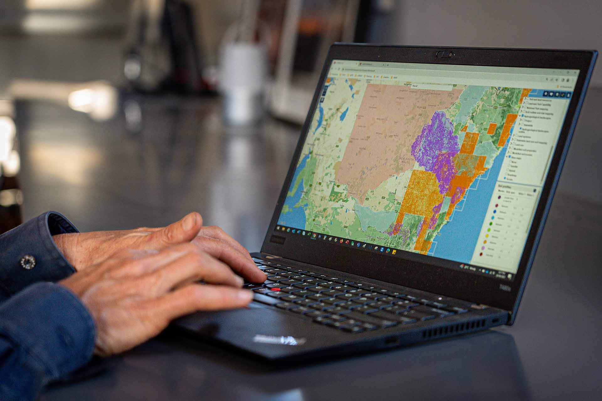 Person using a laptop displaying a colorful geographic information system (GIS) map