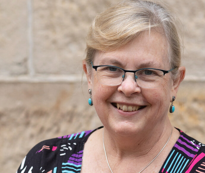 Portrait of a professional woman, smiling confidently. She is standing in front of a brick wall. 