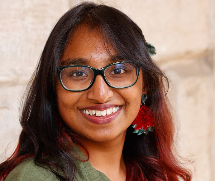 Portrait of a woman, smiling confidently. She is in front of a stone wall. 