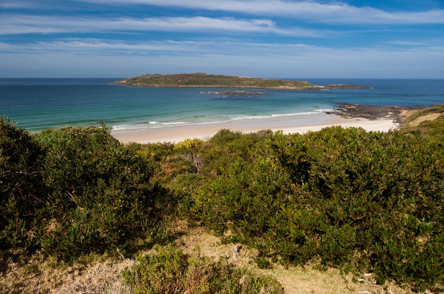 A serene landscape of Murramarang Aboriginal Area, including lush green vegetation, white fine sand and glistening ocean in various shades of blue.