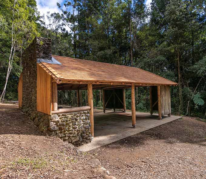 A stone and wood shelter with a pitched roof in a forested area