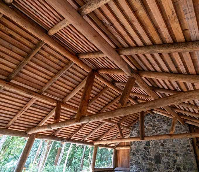 A wooden beam ceiling with an intricate pattern of supporting beams above stone walls