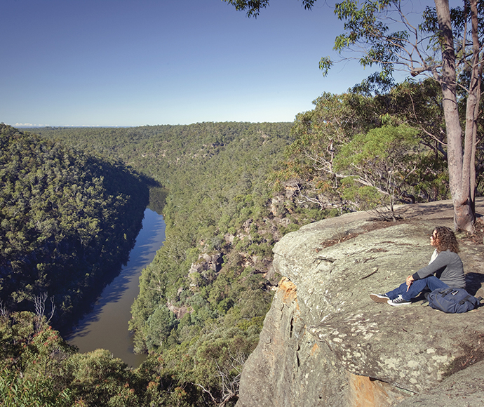 Woman sitting on a rock overlooking a steep gorge with a river running through it and trees either side.