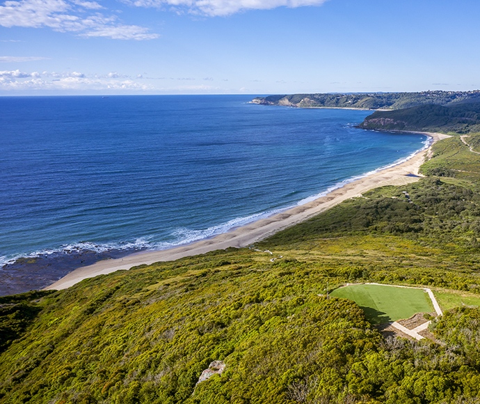 A picturesque beach scene featuring gentle waves and a charming house situated atop a hill in the background.