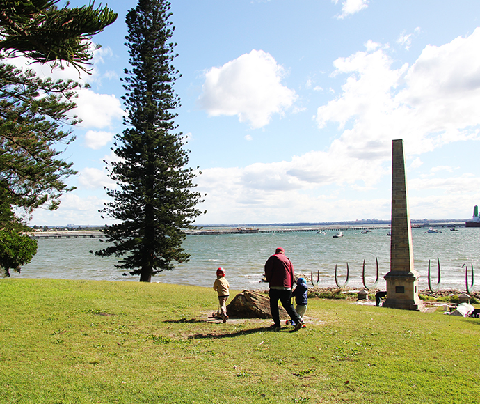 Man and a child walking along a grassy area looking out at the Sculptures along Burrawang walk, Kurnell Area, Kamay Botany Bay National Park.