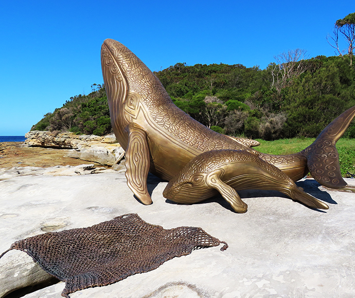 Sculpture titled 'The Whales and Rock Weave,' depicting flowing whale forms intertwined with rock elements. Set on the beach at Kamay Bay.