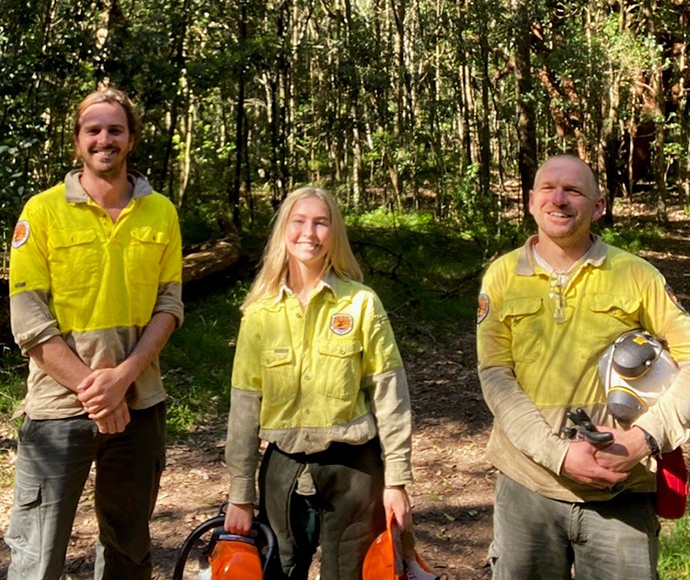 Three people in yellow uniforms with safety gear in a forest.