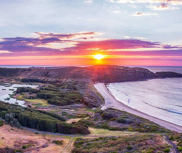 Sunset over a coastline with a beach, greenery, and water inlets.