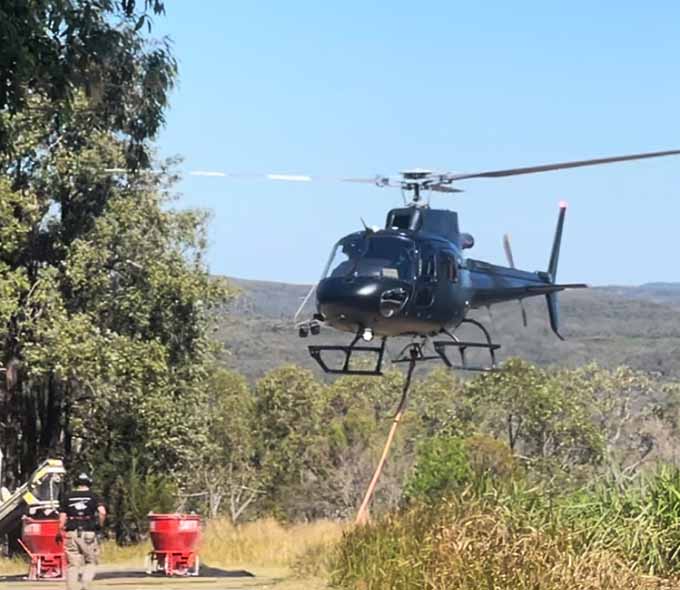 A helicopter hovers above the ground near equipment 