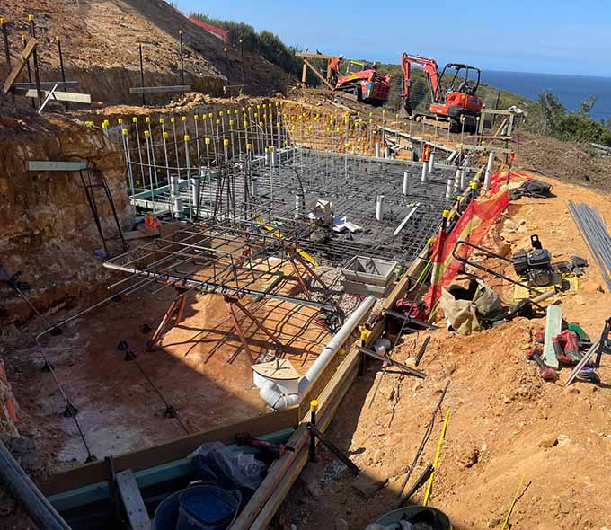 A construction site with foundational steel framework, machinery, and materials near a body of water