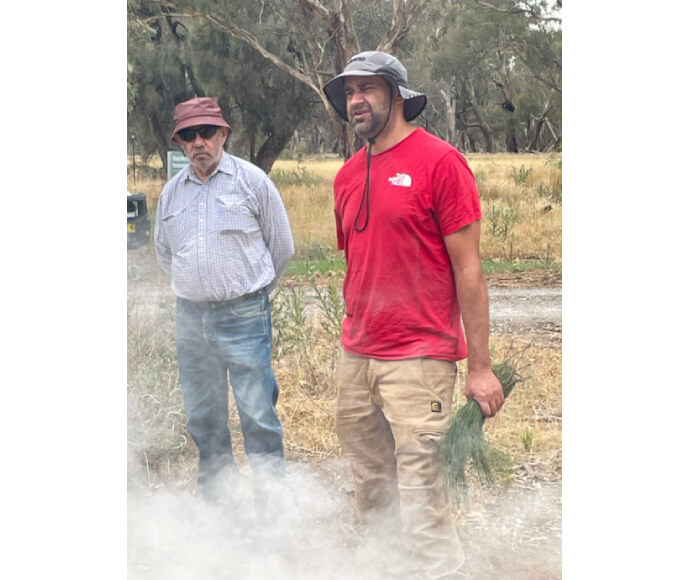 Members of the Bangerang nation Kevin and Roland Atkinson share their knowledge with Murray and Lower Darling EWAG members. Roland was holding a thick bunch of grasses in his hand as smoke rises from an unseen source.