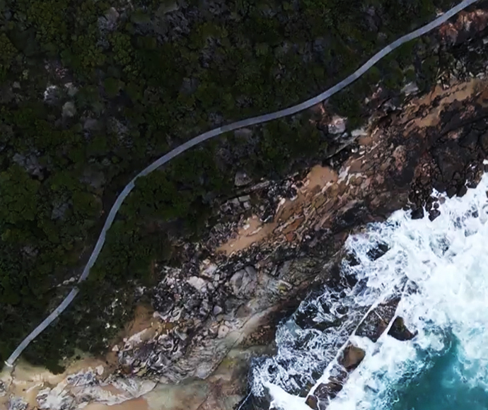 Aerial view of Royal Coast Track. The bushland is on one side and waves are crashing on the other.