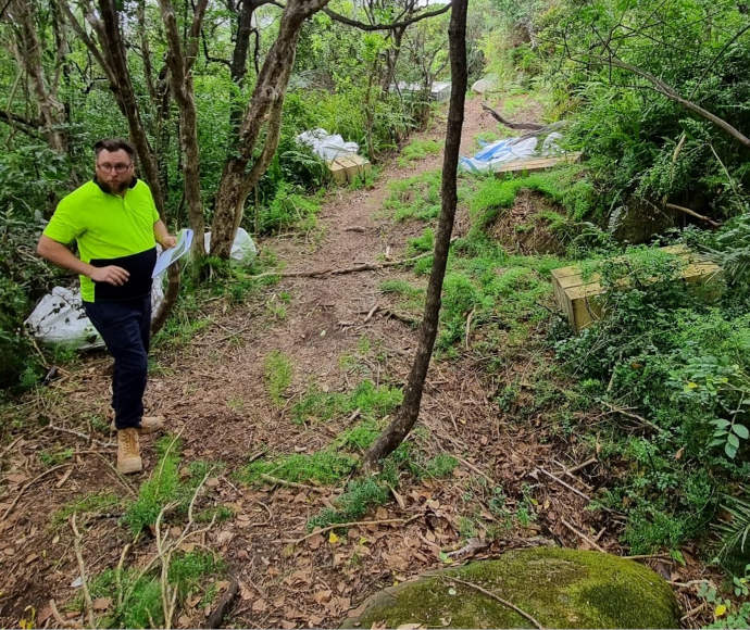 A workmen in a fluorescent t-shirt stands looking thoughtfully on a dirtpath among vivid foliage