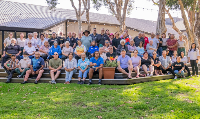 Large group of people siting and standing on a green lawn with a building behind them.