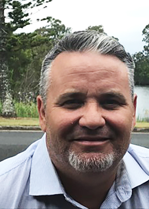 Image shows a man smiling with short hair and a blue shirt