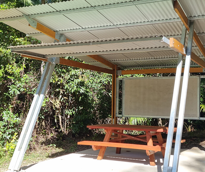 Interpretation shelter at Bindarri National Park, featuring a sloped steel roof, a wooden bench, an informational panel, and surrounded by lush greenery.