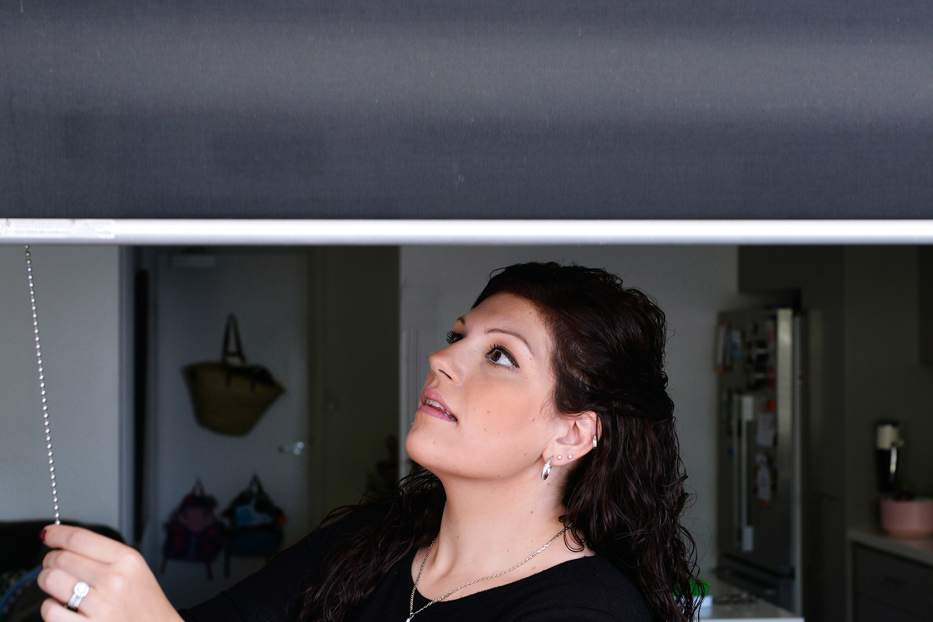 A woman closing black blinds via a cord