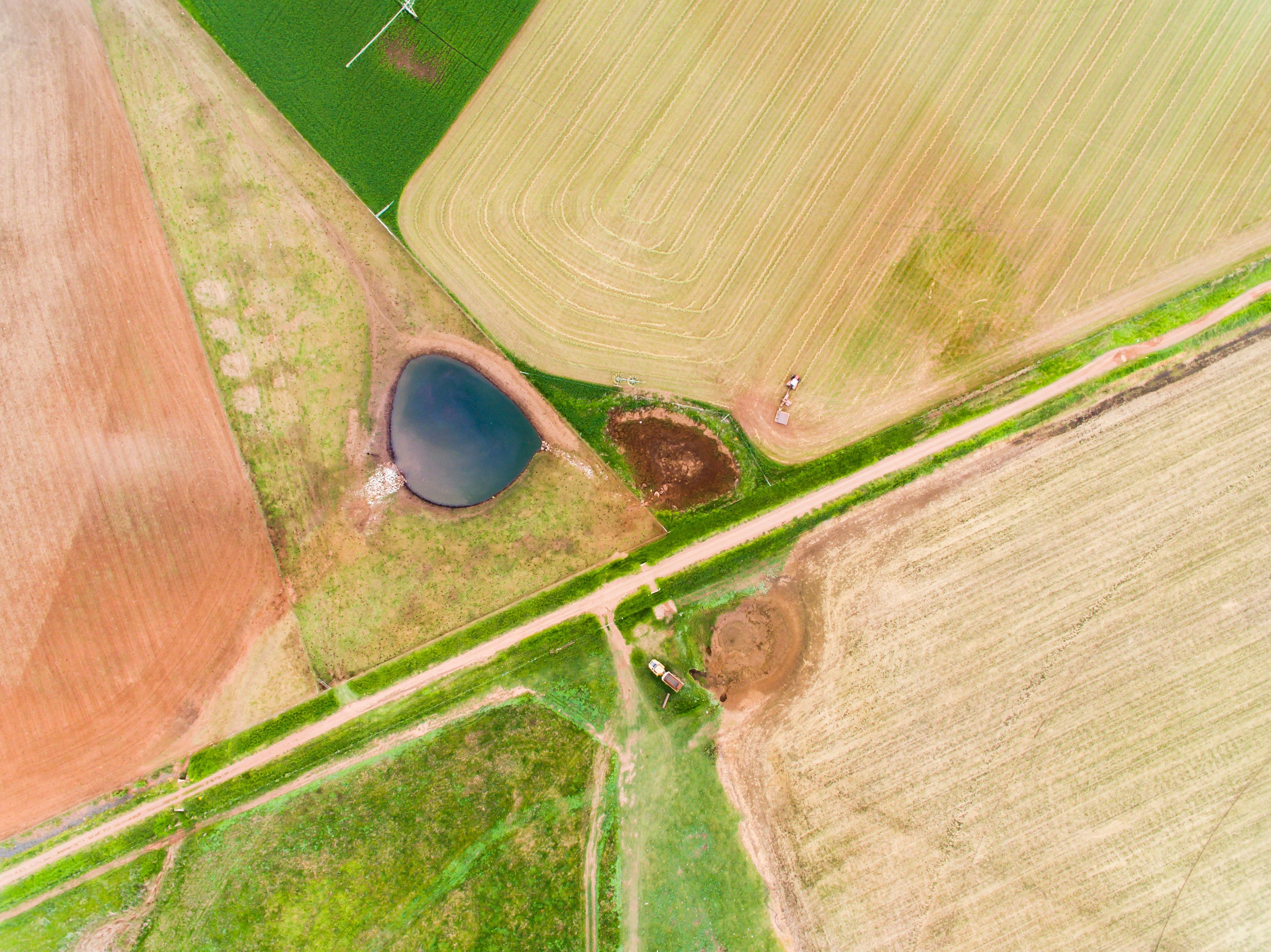 An aerial panorama of Bylong Valley in rural NSW, showcasing a patchwork of cropped fields in varying colors of brownish-red, brownish-yellow, and green. The fields are arranged side by side, creating a vibrant mosaic of agricultural land.