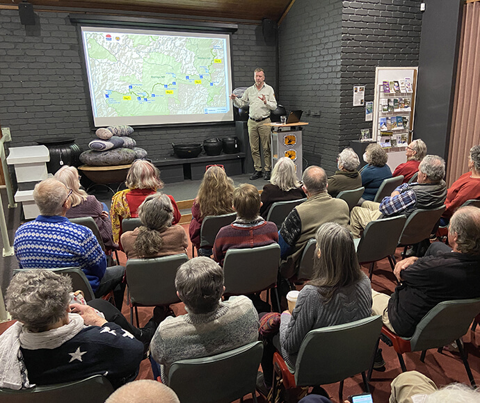 Glenn Storrie addressing a community briefing at the Dorrigo Rainforest Centre, with a seated audience and informational displays in the background.