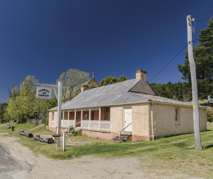 Historic building with a weathered tin roof and chimney, labelled "Farmer's Inn," surrounded by greenery under a clear blue sky, conveying nostalgia.