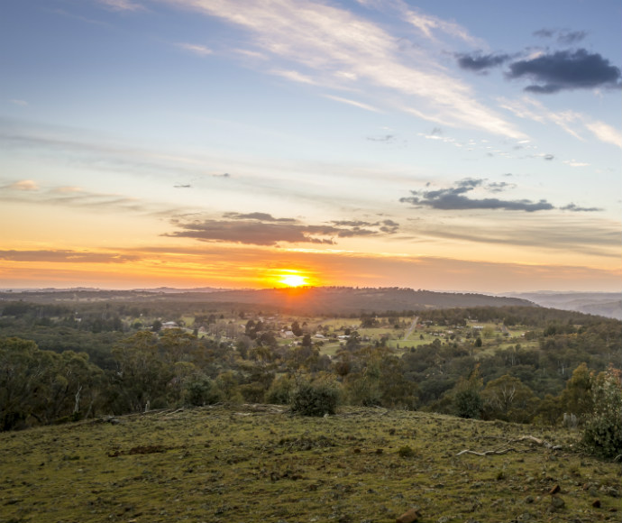 Sunset over a hilly landscape with a vibrant orange sky and scattered clouds. Rolling hills covered in green vegetation convey a serene and peaceful mood.