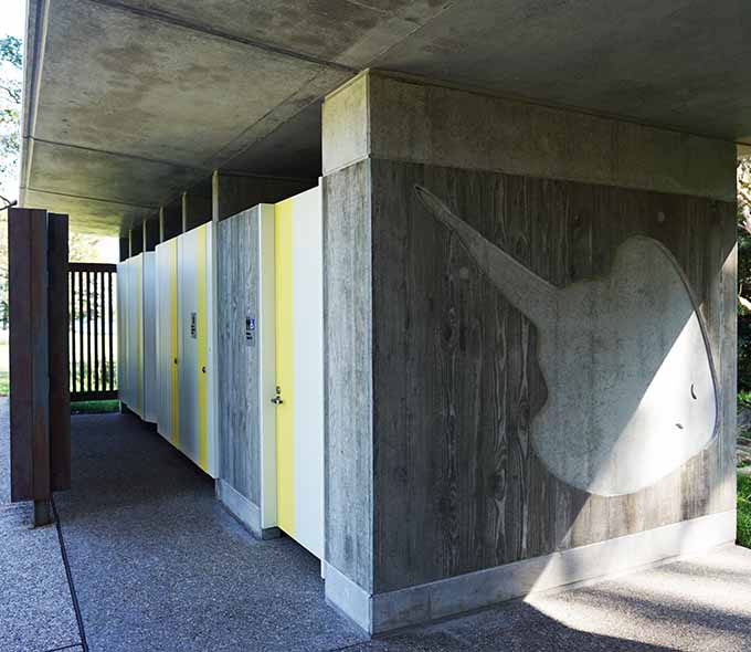 Newly installed amenities at Kamay Botany Bay National Park's Commemoration Flat. Modern facilities, including toilets are surrounded by lush greenery. The area is clean and well-maintained and features abstract stingray artwork on one of the walls.