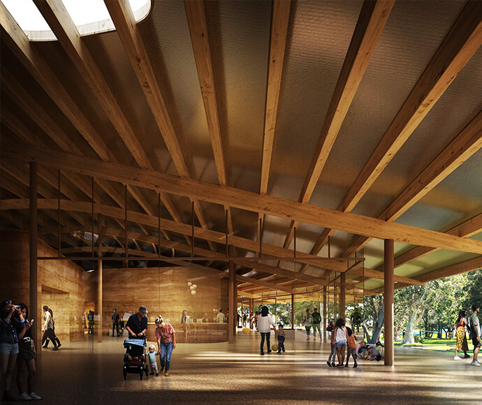 The image shows the interior of a modern building with a high ceiling supported by wooden beams. The space is open and spacious, with large glass windows allowing natural light to flood in. Several people are walking or standing around, including a person pushing a stroller and a child holding hands with an adult. In the background, there's a reception or information desk, and beyond the windows, you can see trees and greenery.