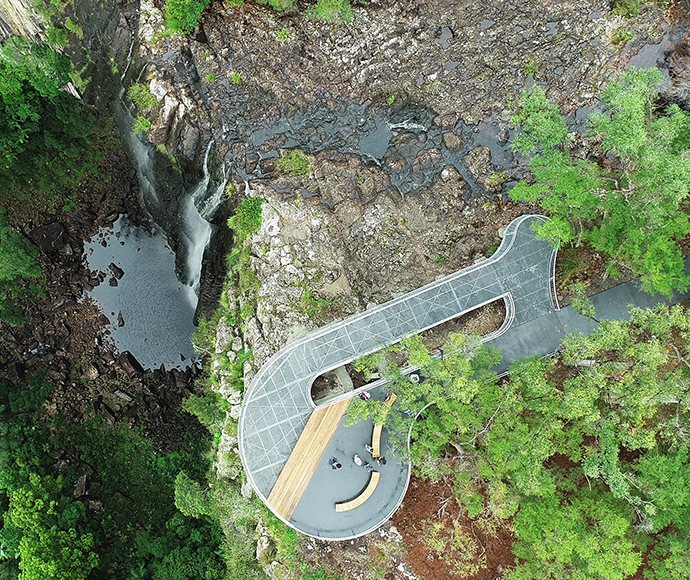 Aerial view of Minyon Falls Lookout in Nightcap National Park, showcasing the waterfall cascading into a deep gorge surrounded by lush, green rainforest.