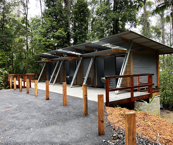 Outdoor rest area with benches and metal roof shelters in a forest setting.