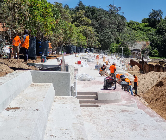 A number of workmen working on concrete bleachers by a thick treeline