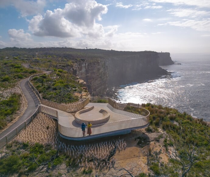 Aerial view of a couple standing at the Yiningma Lookout of Sydney Harbour National Park, offering panoramic views of the harbour and surrounding natural landscape.