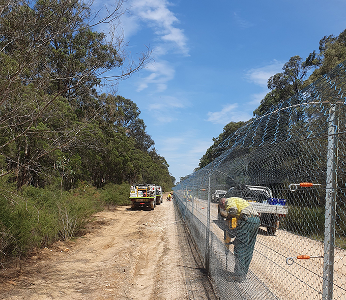 Workman fixing skirt of mesh fence to ground.