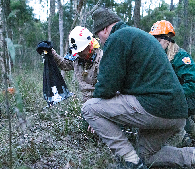 Three NPWS officers kneeling with bag.