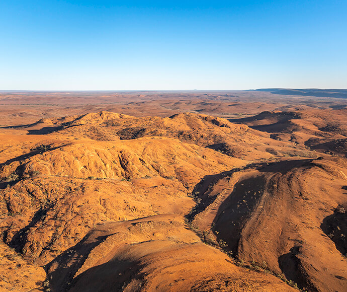 An aerial photo of Mutawintji National Park, featuring vibrant red rocky ranges with no vegetation under a clear sky.