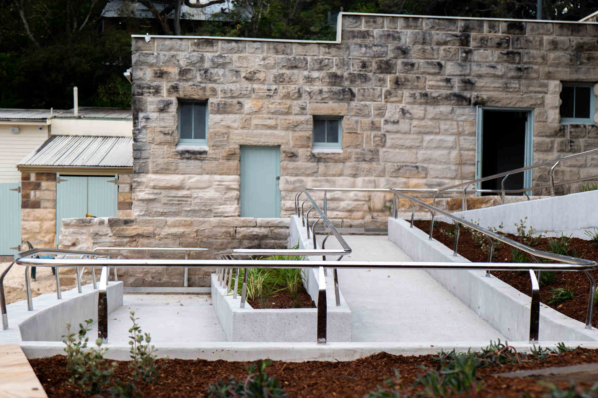 A twisting ramp with shining metal guard rails in front of a stone building